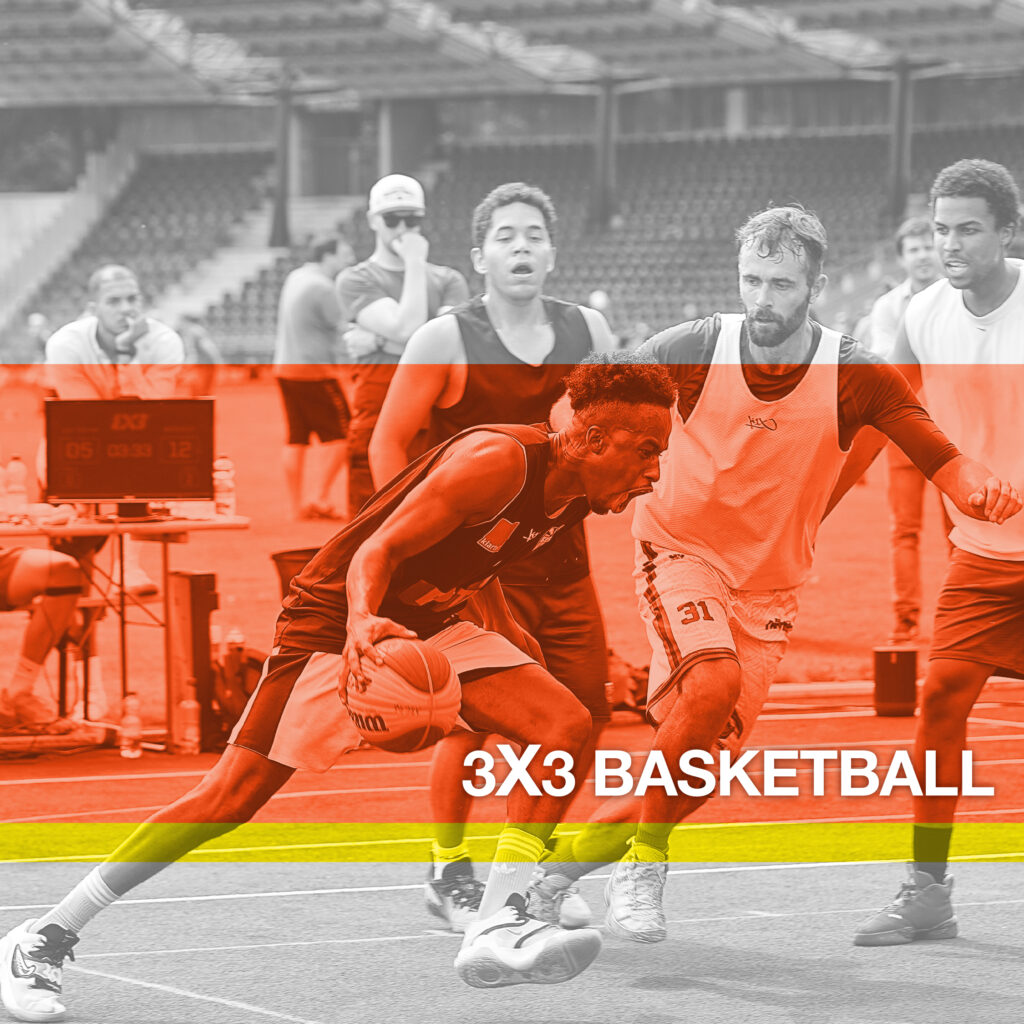 Zwei Mannschaften spielen 3x3-Basketball auf einem Außenplatz. Ein Spieler dribbelt, während die anderen ihm folgen und verteidigen. Im Hintergrund sind eine Anzeigetafel und leere Tribünen zu sehen. Das Bild ist teilweise mit orangefarbenen und gelben Bändern und dem Text „3X3 BASKETBALL“ überlagert.