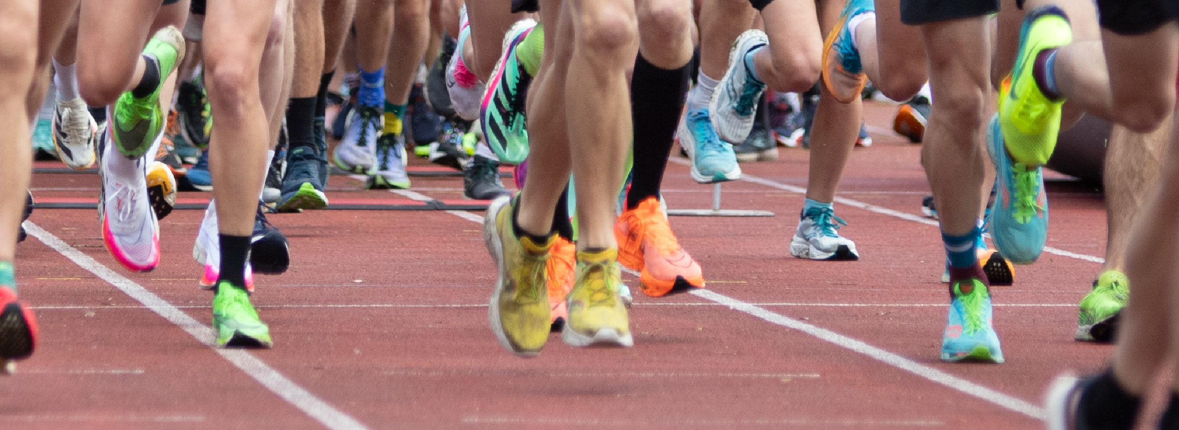 Nahaufnahme der Beine und Füße von Läufern in verschiedenen bunten Laufschuhen, während sie bei einem Laufen-Event auf der Laufbahn rennen.