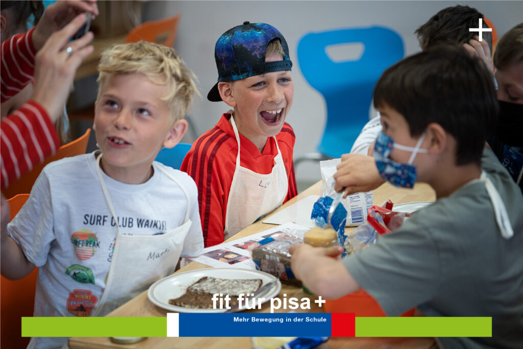 Kinder sitzen an einem Tisch, eines trägt eine Mütze und lächelt. Sie beschäftigen sich mit Zeitungen, Snacks und lernen etwas über Ernährung. Text: „fit für pisa+ Mehr Bewegung in der Schule.“.