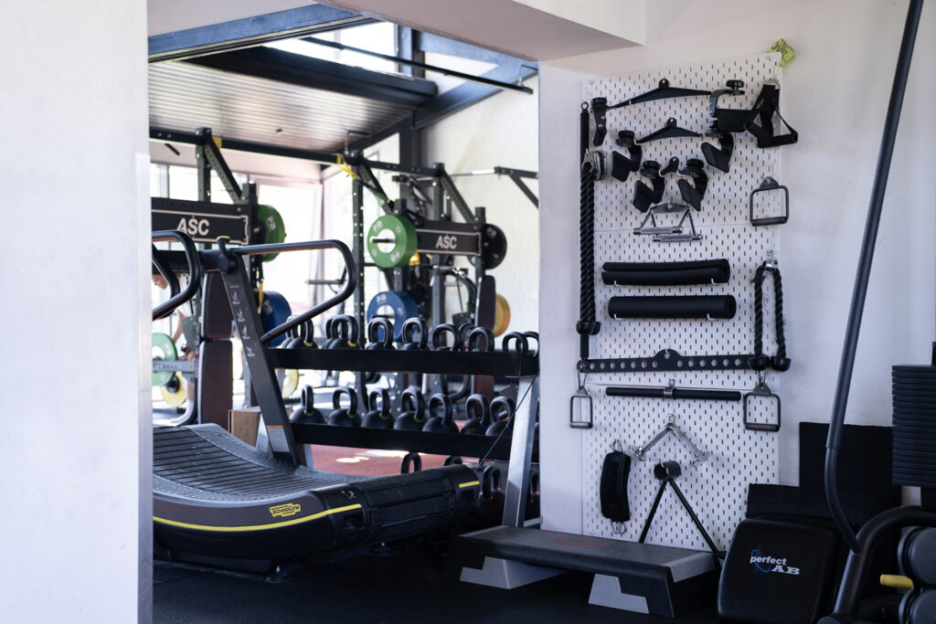 Ein auf Leistung ausgelegtes Fitnessstudio mit Laufband, Kettlebells, Gewichthebegeräten und verschiedenen Trainingsgeräten, die übersichtlich an einer Wandtafel angebracht sind.