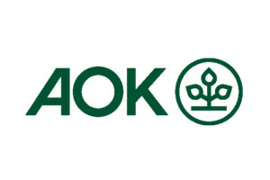 Grüne Buchstaben "AOK" neben einem kreisförmigen Emblem mit einer stilisierten Pflanze mit drei Blättern und einem Stängel in der Mitte auf weißem Hintergrund - ein Symbol für Gesundheit und Wohlbefinden, das oft im Zusammenhang mit Laufen-Initiativen gesehen wird.