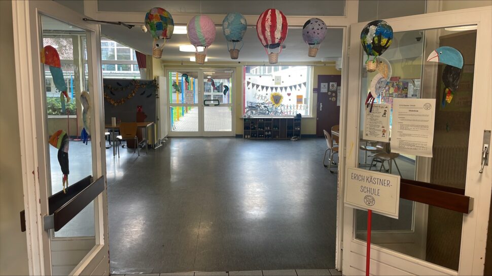 Blick durch offene Flügeltüren in einen Schulflur, der mit bunten Papier-Heißluftballons und festlichen Girlanden geschmückt ist; auf einem Schild steht „Erich-Kästner-Schule“.